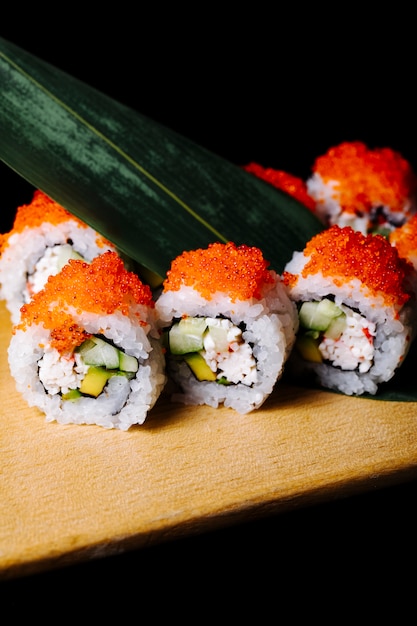 Sushirollen mit rotem Kaviar und grünem Blatt auf einem hölzernen Brett.