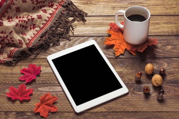 Tablet und Decke in der Nähe von Blättern und Kaffee