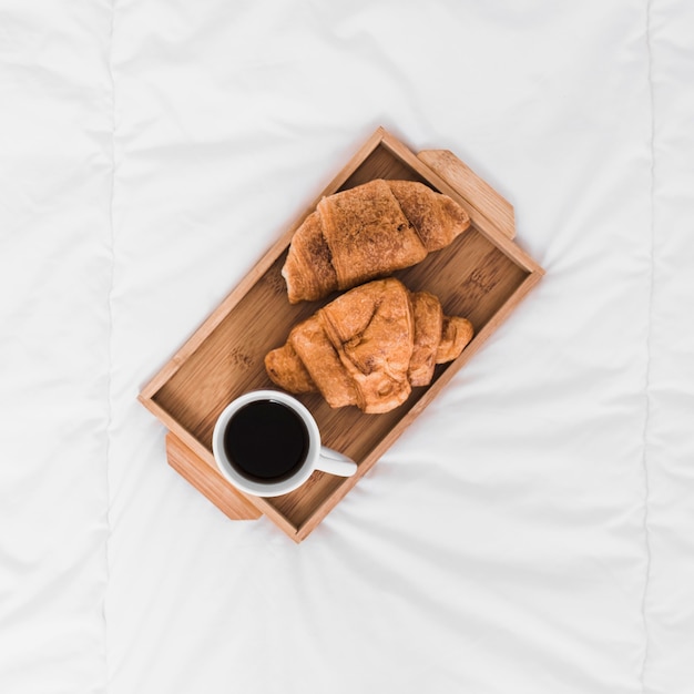 Tablett mit Croissants und Kaffee auf dem Bett