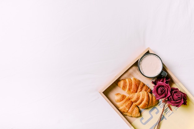 Tablett mit Croissants und Rosen auf dem Bett