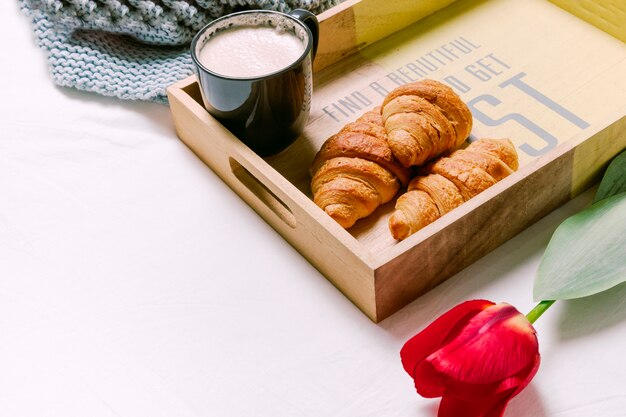 Tablett mit Hörnchen und Tasse Milch auf hellem Bett