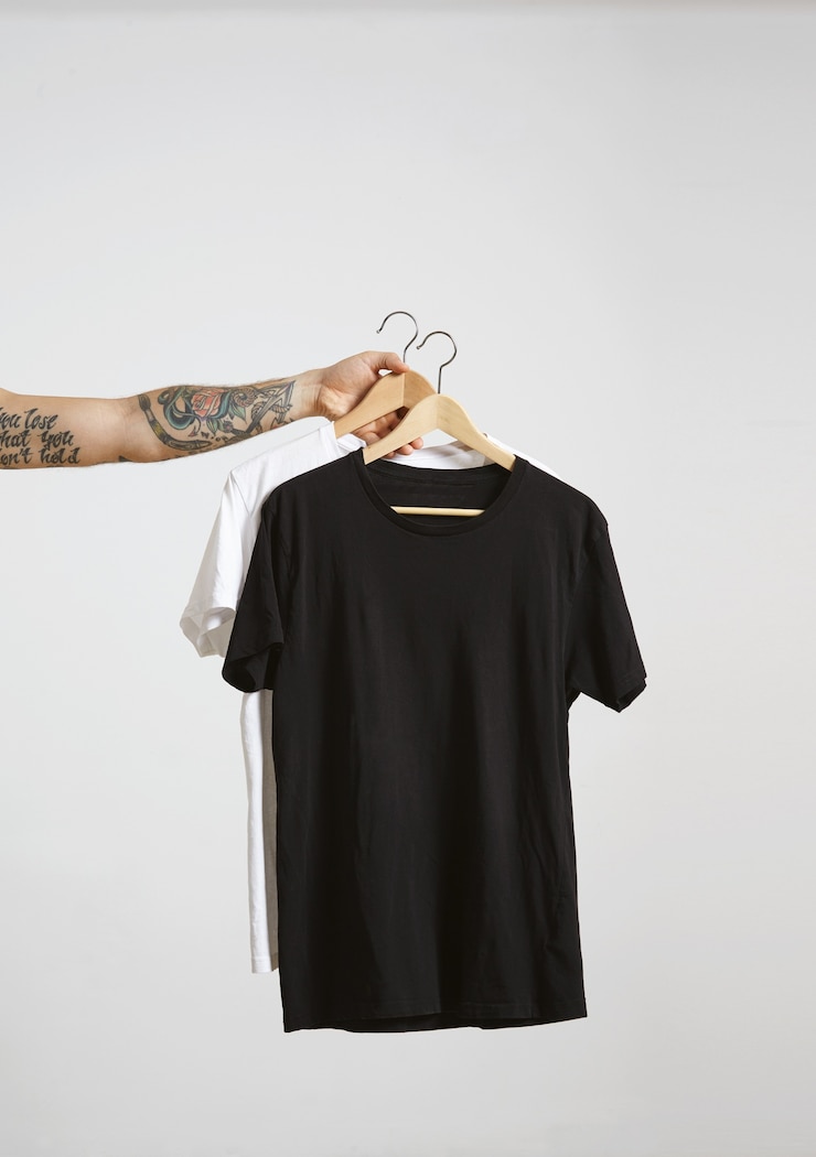 Kostenlose Foto tätowierte bikerhand hält holzhänge mit leeren schwarzen und weißen t-shirts aus hochwertiger dünner baumwolle, isoliert auf weiß
