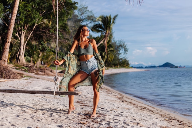 tätowierte kaukasische Frau in Jeansshorts und grünem trendigem Crop-Top