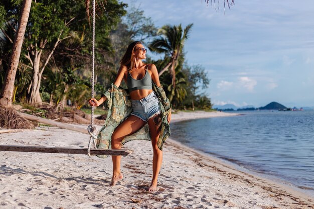 tätowierte kaukasische Frau in Jeansshorts und grünem trendigem Crop-Top