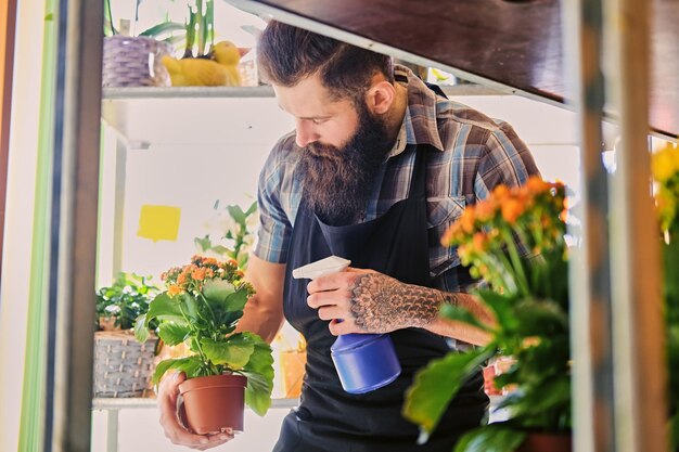 Tätowierter bärtiger Mann, der Blumen in einem Marktgeschäft gießt.