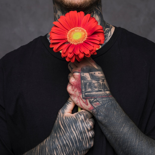 Tätowierter junger mann, der in der hand rote gerberablume hält