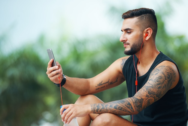 Tätowierter Sportler mit Telefon draußen