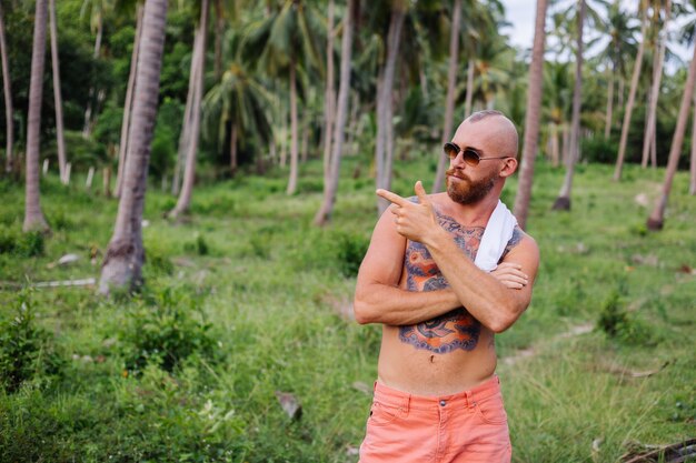 Tätowierter starker Mann auf tropischem Dschungelfeld ohne Hemd