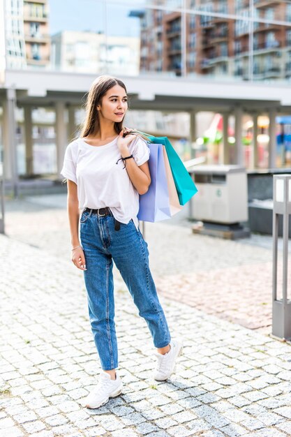 Tag einkaufen. Volle Länge der jungen Frau, die Einkaufstaschen hält und beim Gehen entlang der Straße lächelt