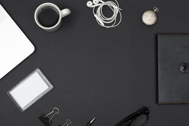 Tagebuch; Kopfhörer; Kaffeetasse; Laptop; Büroklammern; Brillen auf schwarzem Desktop
