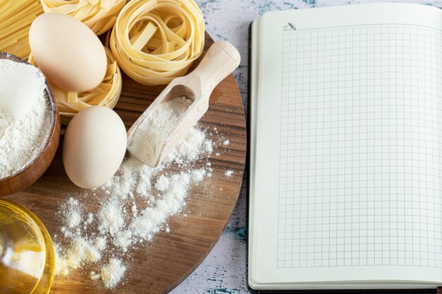 Tagliatelle mit Öl, Ei und Mehlschale auf Holzbrett und Notizbuch.
