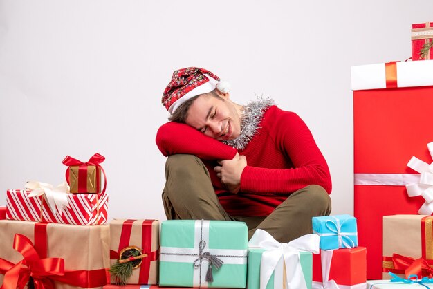 Tagträumer junger Mann der Vorderansicht mit Maske, die um Weihnachtsgeschenke sitzt