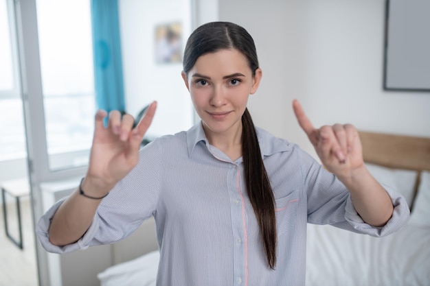 Taillenporträt einer lächelnden attraktiven Frau mit zwei angehobenen Zeigefingern, die für die Kamera posieren