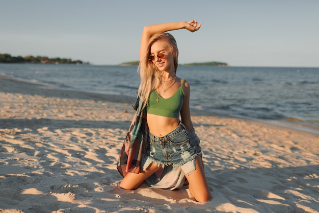Tan schlanke Frau mit langen blonden Haaren, die am tropischen Strand aufwerfen.