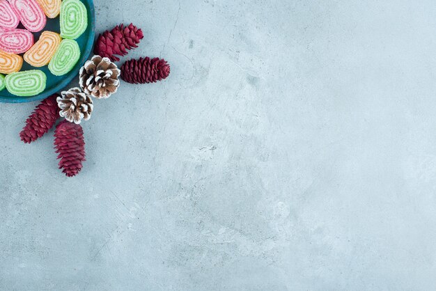 Tannenzapfen mit zuckerhaltigen Fruchtmarmeladen auf blauem Holzbrett.