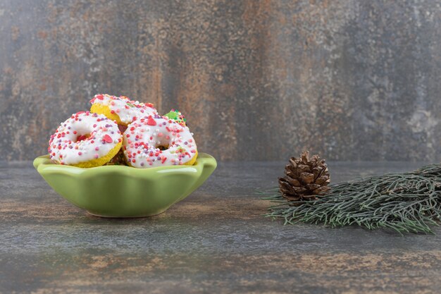 Tannenzweig und ein Kegel neben einer kleinen Schüssel Donuts auf Marmoroberfläche