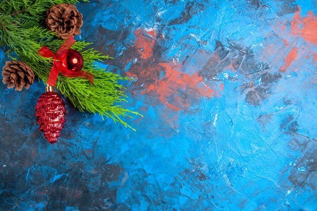 Tannenzweige mit Tannenzapfen und hängenden Ornamenten auf blau-rotem Hintergrund mit freiem Platz