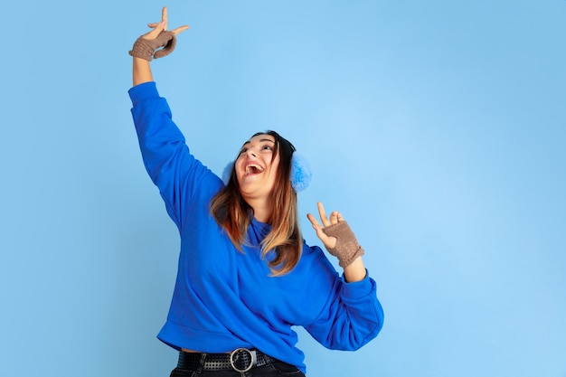 Tanzen. Porträt der kaukasischen Frau auf blauem Studiohintergrund. Schönes weibliches Modell in warmer Kleidung. Konzept der menschlichen Emotionen, Gesichtsausdruck, Verkauf, Anzeige. Winterstimmung, Weihnachtszeit, Feiertage.