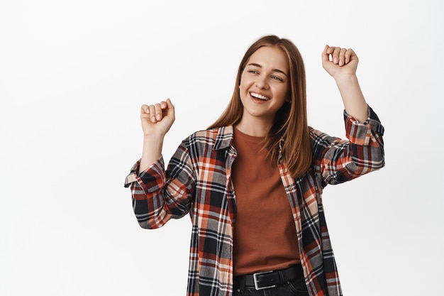 Tanzende Frau, Studentenparty, Spaß auf der Party, Hände heben, lachen und glücklich lächeln, Veranstaltung genießen, zur Musik tanzen, gegen weiße Wand stehen