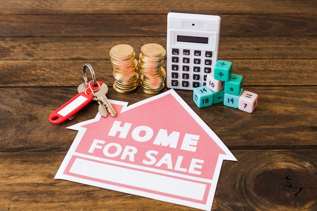 Taschenrechner, Matheblöcke, Staplungsmünzen und Schlüssel mit Haus für Verkaufsikone auf hölzernem Hintergrund