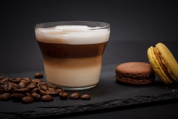 Tasse cappuccino, kaffeebohnen und makronen auf schwarzem hintergrund.