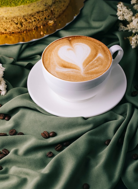 Tasse Cappuccino mit Kaffeebohnen und Kuchen auf dem Tisch