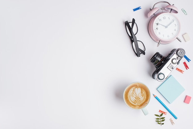 Tasse Cappuccino mit Latte-Art; Vintage Kamera; Wecker; Bleistift und Brille auf weißem Hintergrund