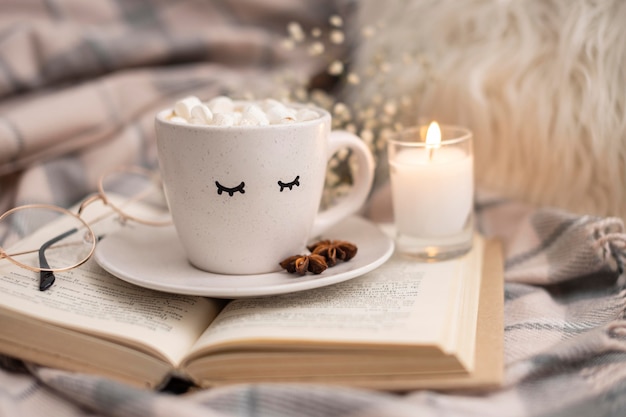 Tasse heißen Kakao mit Marshmallows auf Buch mit Kerze
