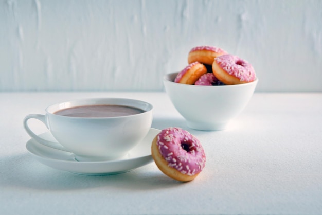Tasse heißen kakao und donuts auf weißem hintergrund. leckere rosa donuts und heiße kakaotasse. süßes frühstück