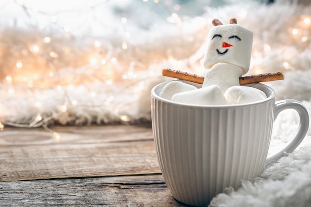 Tasse heißes Getränk mit Marshmallow-Schneemann auf verschwommenem Hintergrund hautnah
