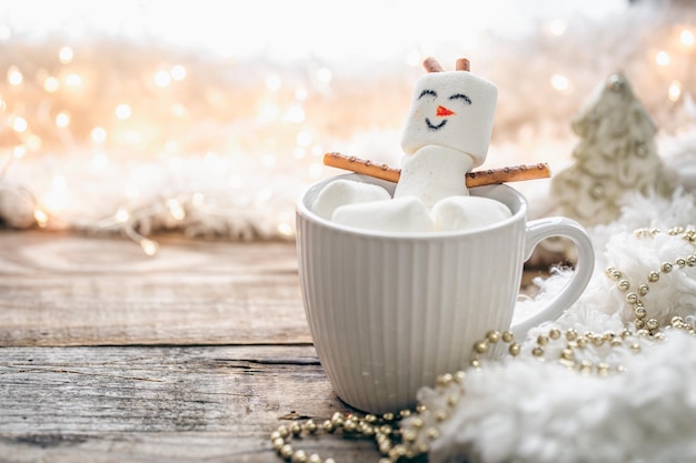 Tasse heißes Getränk mit Marshmallow-Schneemann auf verschwommenem Hintergrund hautnah