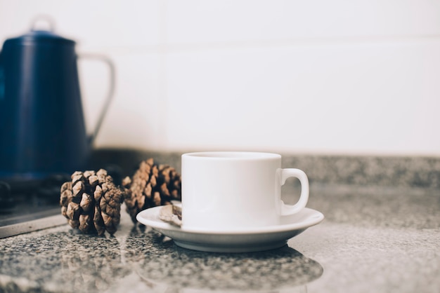 Tasse Kaffee auf Saucer und Tannenzapfen auf Küchentheke gegen weißen Hintergrund