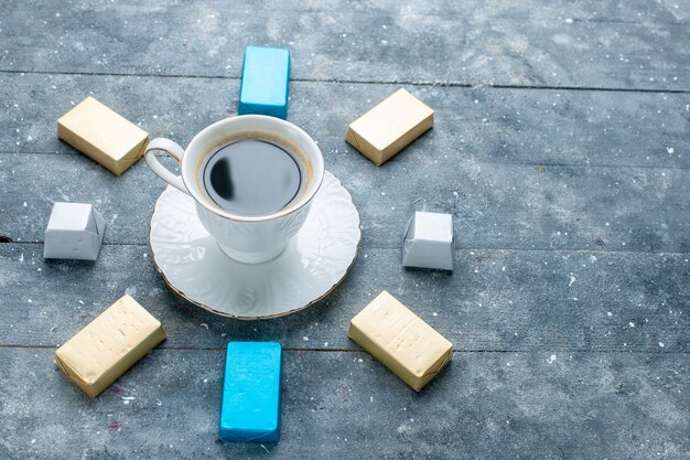 Tasse Kaffee heiß und stark mit gefütterter goldgeformter Schokolade auf hellblauem Schreibtisch, Kaffeekakaogetränk