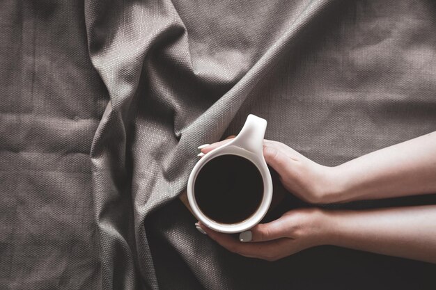 Tasse Kaffee im Bett in weiblichen Händen flach gelegt