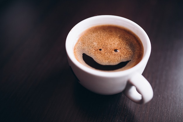 Tasse Kaffee mit Schaum, Lächelngesicht, auf dem Schreibtisch lokalisiert