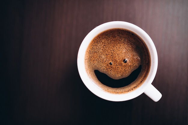 Tasse Kaffee mit Schaum, Lächelngesicht, auf dem Schreibtisch lokalisiert