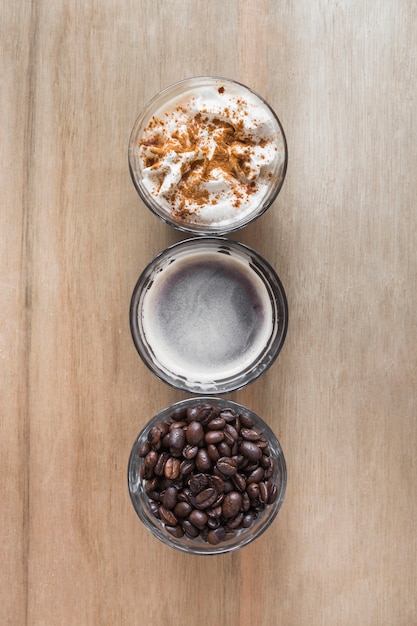 Kostenloses Foto tasse kaffee mit schlagsahne und röstkaffeebohnen auf hölzernem hintergrund