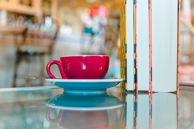 Tasse Kaffee mit stehenden Büchern auf Glastisch