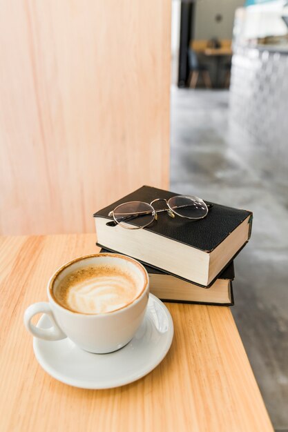 Tasse Kaffee mit Tagebuch und Schauspielen auf hölzernem Schreibtisch