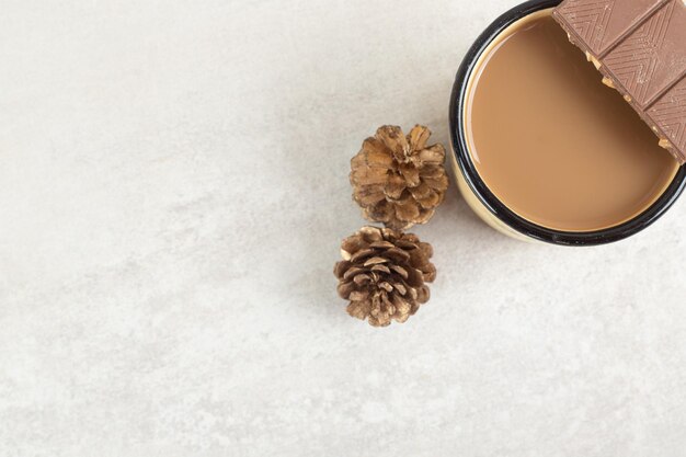 Tasse Kaffee mit Tannenzapfen und Schokoriegel.