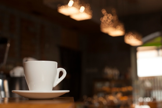 Tasse Kaffee mit Untertasse auf Tabelle mit defocus Caféhintergrund