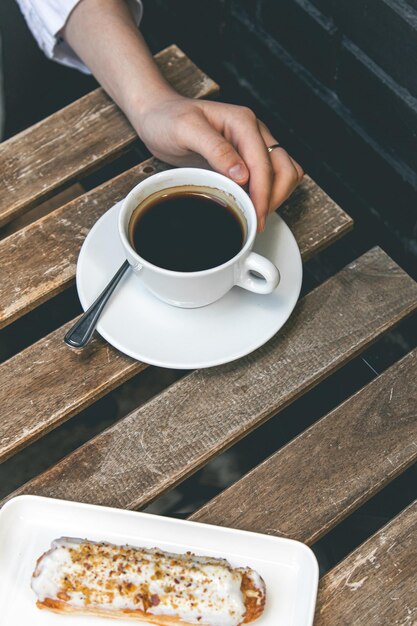 Tasse Kaffee und Eclair auf einer Holztischnahaufnahme