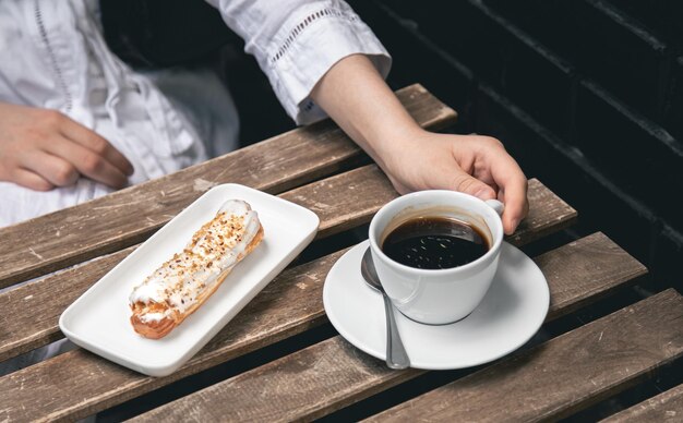 Tasse Kaffee und Eclair auf einer Holztischnahaufnahme