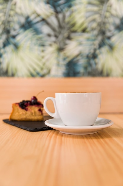 Tasse Kaffee und Gebäck auf hölzernem Schreibtisch