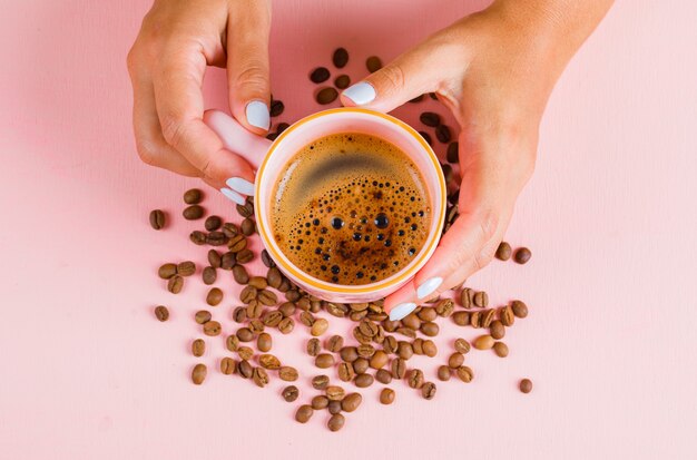 Tasse Kaffee und Kaffeebohnen auf rosa Oberfläche