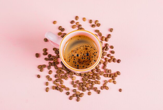 Tasse Kaffee und Kaffeebohnen auf rosa Oberfläche