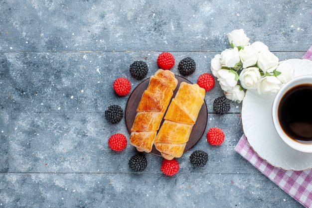 Tasse Kaffee zusammen mit süßen leckeren Armreifen und Beeren auf grauem Schreibtisch, süßer Gebäckzuckerkuchen