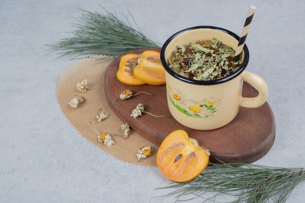 Tasse Kräutertee, Blumen und Kaki-Scheiben auf Holzbrett. Hochwertiges Foto