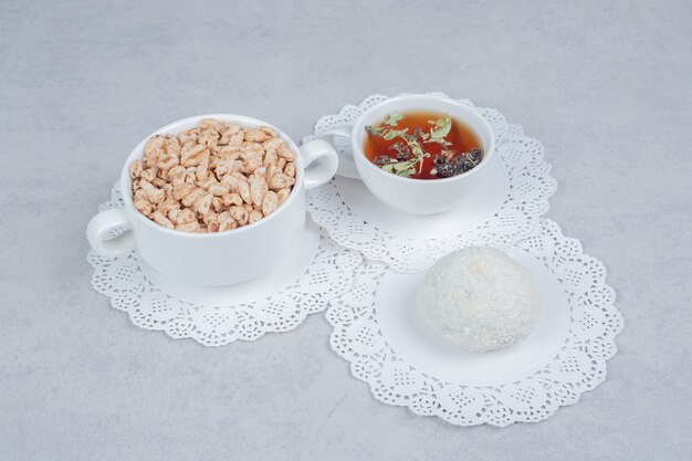 Tasse Kräutertee, Kokosnusskeks und Schüssel mit Süßigkeiten auf weißem Tisch. Hochwertiges Foto