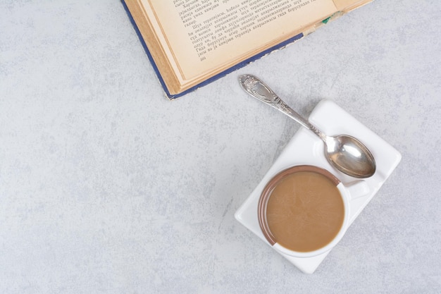 Tasse Milchkaffee, Löffel und Buch auf Steinoberfläche. Foto in hoher Qualität